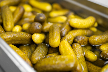 Close-up of pickled cucumbers in brine, showing glossy texture and varied shades of green,...