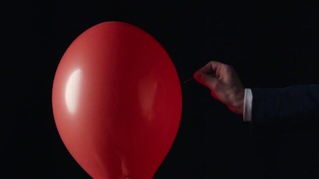 Hand popping red balloon with pin closeup on black background. Happy birthday