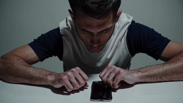 Young man intensely focused on his smartphone, seemingly captivated and isolated on a white background, possibly suggesting digital addiction or imprisonment