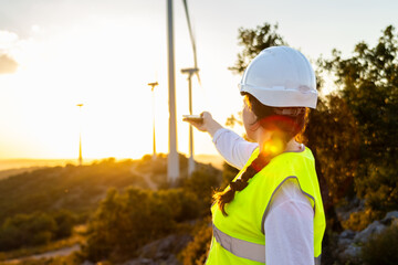 Female engineer pointing at wind turbines during sunset at wind farm