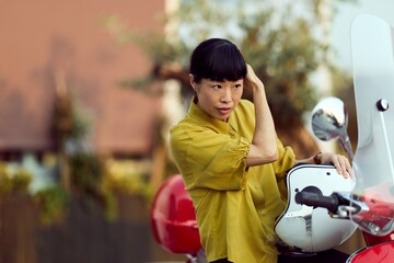 Woman Fixing Hair While Sitting on a Red Scooter Outdoors