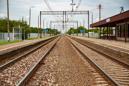 Empty railway station with parallel train tracks leading into the distance. Symmetrical perspective and calm atmosphere on a quiet day