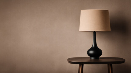 A modern black table lamp with a beige shade sits on a wooden table against a textured beige wall.