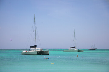 Sailboats anchored in bright turquoise waters under a clear blue sky near a tropical beach