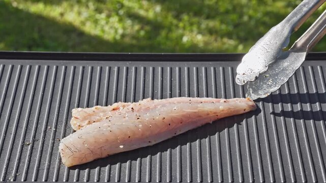 outdoor cooking. cook preparing fresh sea bream fish fillet with spices on hot grill pan for making delicious meal in garden, food closeup, outdoors natural light