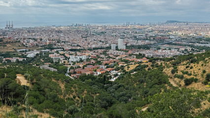 Wide-Angle View of Barcelona's Urban Landscape with Lush Green Hills in the Foreground and the Sparkling Mediterranean in the Distance
