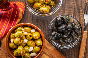 Tapas. Flavored pickled olives in bowl on wooden table. Top view.
