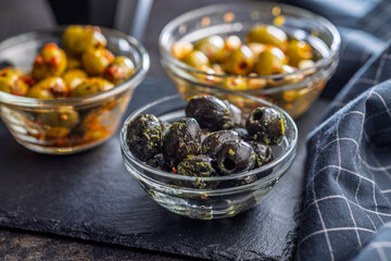 Tapas. Flavored pickled olives in bowl on black table.