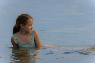 A happy young girl emerges from the water with her eyes shut and a wide smile, causing a big splash...