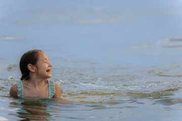 A happy young girl emerges from the water with her eyes shut and a wide smile, causing a big splash...