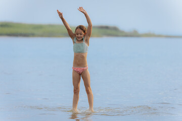 A young girl jumps high above the water in a powerful split pose, splashing below on a bright summer day, capturing motion, freedom, and joy.