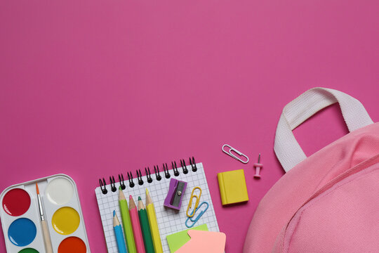 A backpack with colorful school supplies on a color pink background. Top view, space for text