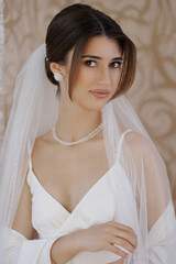 Elegant bride in beautiful wedding attire smiles softly for the camera in a decorated space