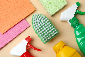 Various cleaning products including brush, sponge, spray on beige background. Flat lay cleaning concept with copy space for text or design