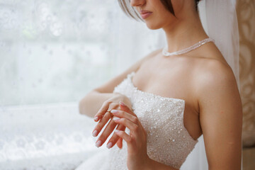Bride preparing for wedding while adjusting her ring near window in soft light