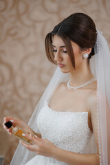 Bride preparing for wedding day while holding perfume in elegant bridal suite