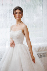 Elegant bride in a stunning white gown posing near a window with soft natural light