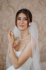 Bride holding perfume and smiling in elegant indoor setting before wedding ceremony