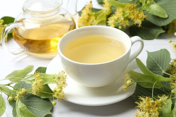 Teapot and cup with linden tea and flowers on wooden table 
