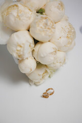 Elegant floral bouquet with wedding rings on a white surface captured in soft light
