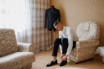 Young man prepares for an event by putting on shoes in a well-decorated room