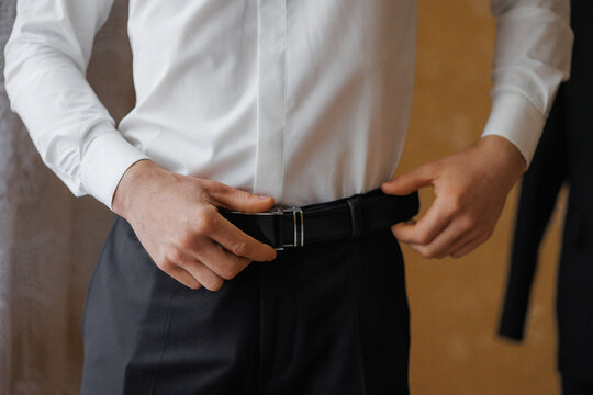 Man adjusting his belt while preparing for a formal event indoors