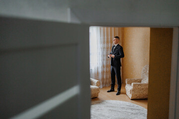 Groom prepares for wedding in elegant suit before ceremony in stylish room with natural light