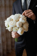 Elegant white peony bouquet held by a groom during a wedding ceremony