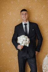Groom standing confidently with bouquet in hands in elegant indoor setting