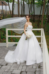 Bride poses elegantly in wedding dress with flowing veil surrounded by greenery