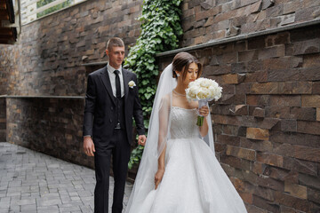 Couple walking together in elegant wedding attire near stone wall