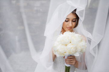 Bride holding bouquet of white peonies while wearing veil in elegant indoor setting