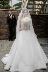 Elegant bride in wedding gown poses with bouquet while groom stands in the background