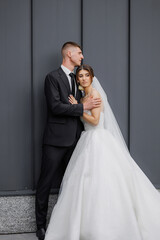 Couple embraces in elegant wedding attire against modern backdrop in daylight