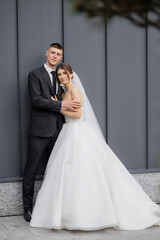 Couple poses together in elegant wedding attire against modern backdrop