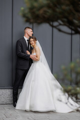 Couple embraces in elegant wedding attire outside modern venue on a joyful day