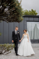 Couple walking hand in hand after wedding ceremony at modern venue during cloudy afternoon