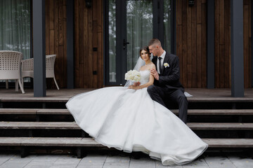 Couple sits on steps in elegant wedding attire, enjoying a moment of intimacy