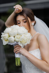 Bride holding white peony bouquet in elegant wedding attire outdoors