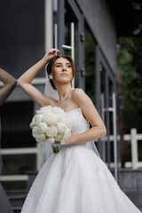 Elegant bride posing with bouquet outside modern venue in daytime