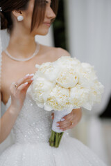 Bride holds beautiful white peony bouquet in elegant dress at outdoor wedding ceremony