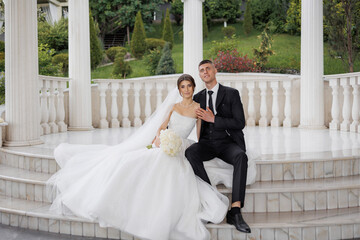Elegant wedding couple posing on marble steps in a lush garden setting