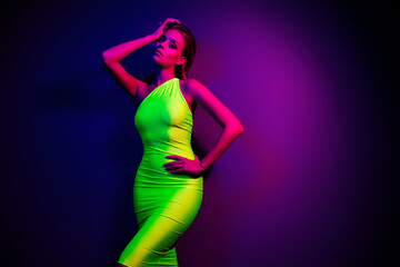Glamorous young woman in a vibrant green dress posing under colorful neon lighting