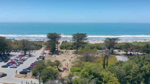 Scenic aerial view of Stintson Beach, California, USA, showing people enjoying a sunny day at the beach, with parking and a snack bar nearby.