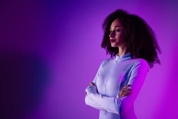 Confident young woman with curly hair wearing a stylish bodysuit standing against a vibrant purple neon background