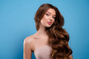 Attractive young woman with long wavy brown hair posing on light blue background in studio