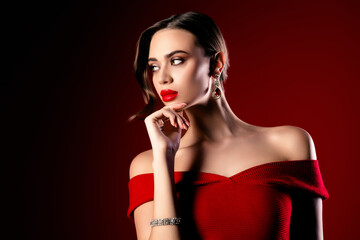 Elegant young woman in a red off-shoulder dress, posing stylishly with chic jewelry in a vibrant studio setting