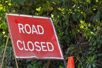 Red 'Road Closed' Traffic Sign in Street With Green Hedge in Background