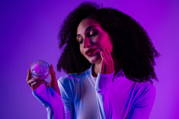 Young African American Woman in Neon Light Holding Cosmetics Jar, Showcasing Skincare and Style in Trendy Purple Hues