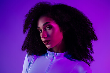 Trendy woman in a stylish jumpsuit illuminated by neon lights against a violet background, expressing beauty